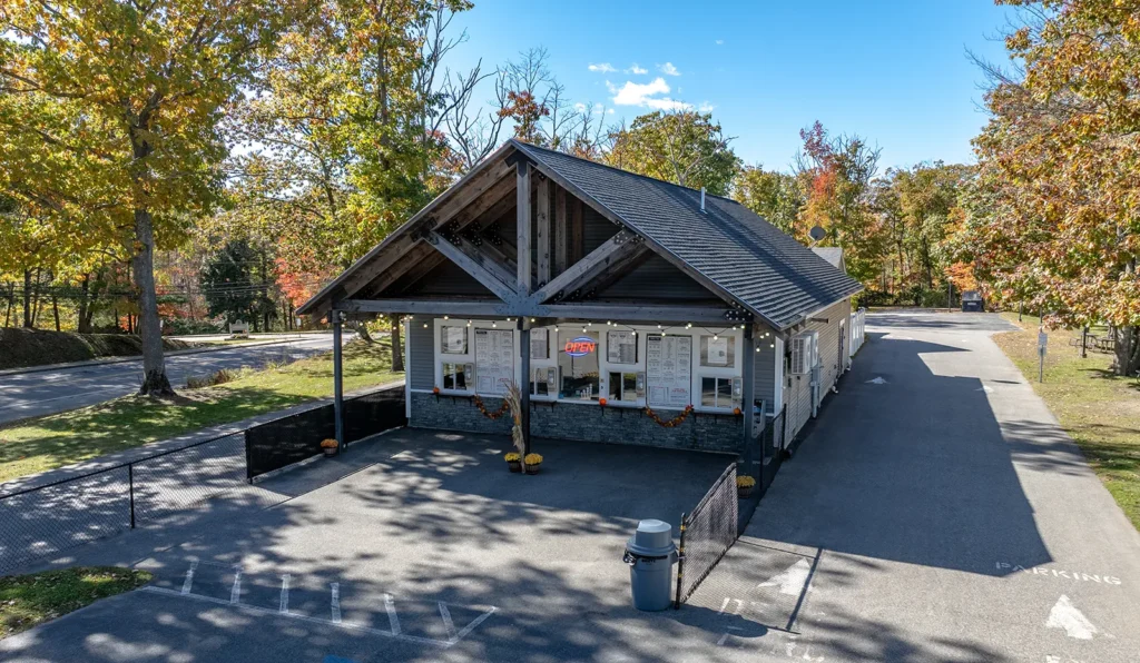 Rustic roadside building with autumn trees and an Open sign, surrounded by a parking area and scenic foliage.