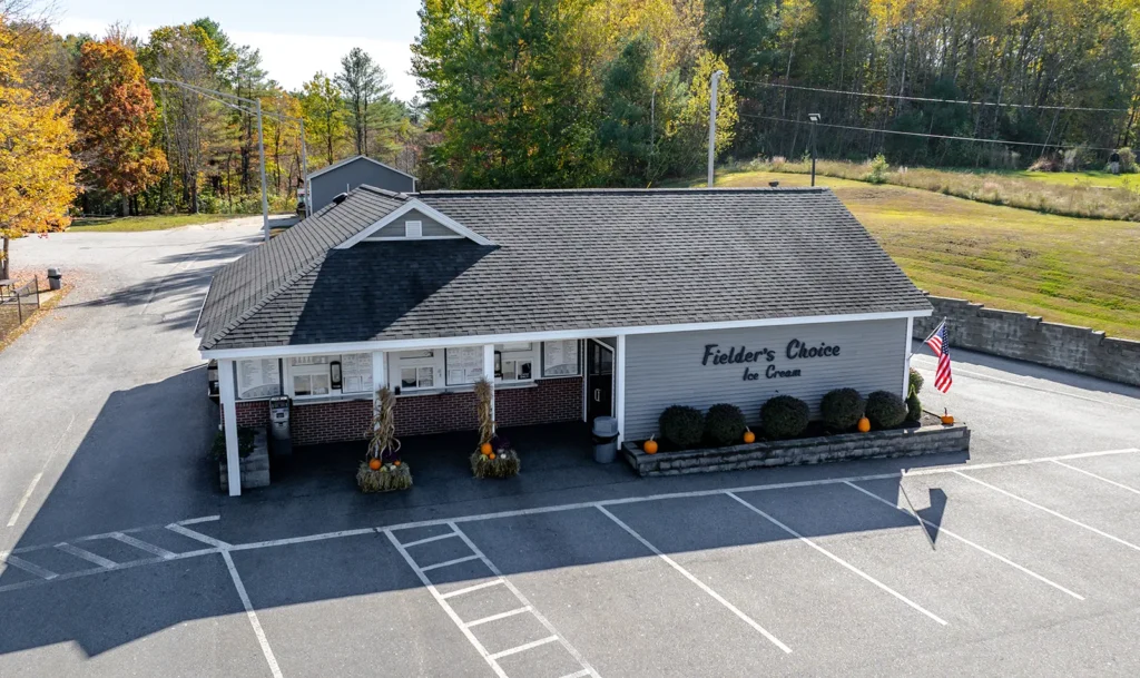 Small ice cream shop with autumn decor in a rural setting, featuring pumpkins and an American flag.