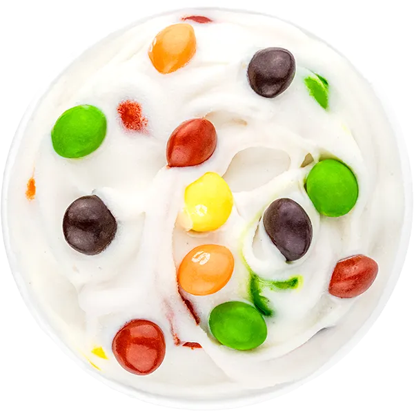 Colorful candy pieces on creamy white ice cream swirl, top view dessert close-up.