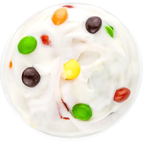 Colorful candy pieces on creamy white ice cream swirl, top view dessert close-up.