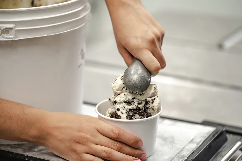 Scooping cookies and cream ice cream into a cup, delicious dessert preparation.