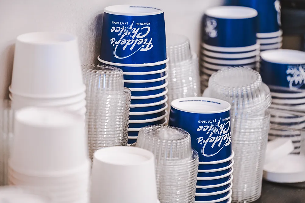 Stacks of blue and white ice cream cups and clear lids on a counter.