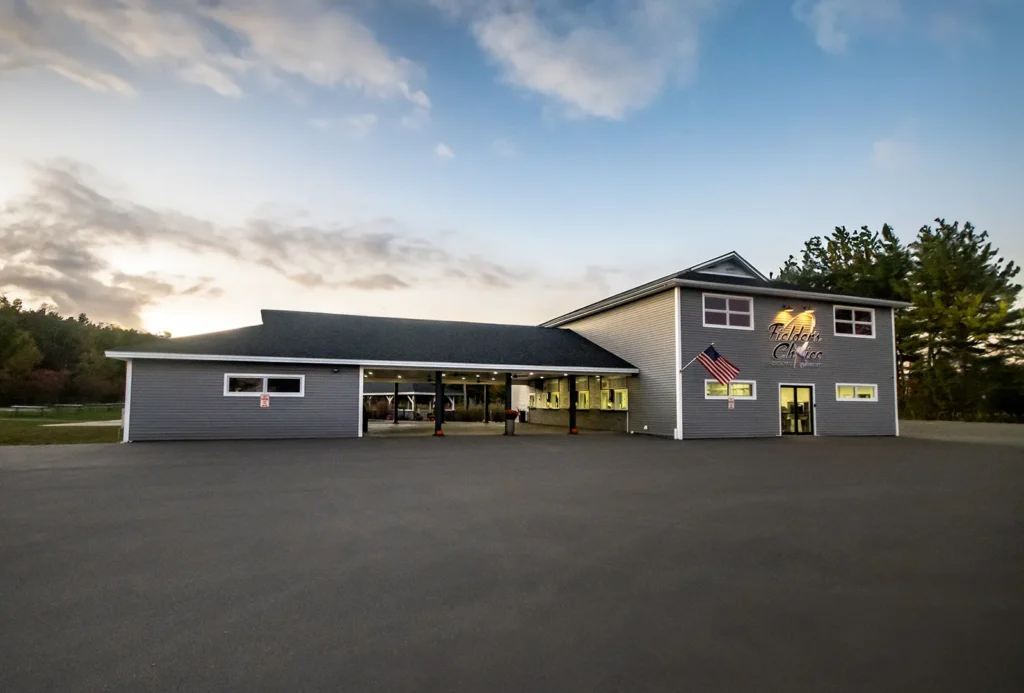 Exterior view of a modern gray building with an American flag, set against a sunset sky and surrounded by trees.