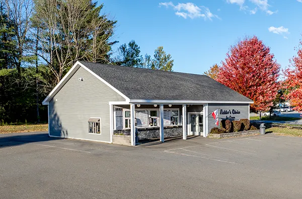 Gray storefront with large windows, surrounded by autumn trees and clear blue sky, located in a quiet, paved area.