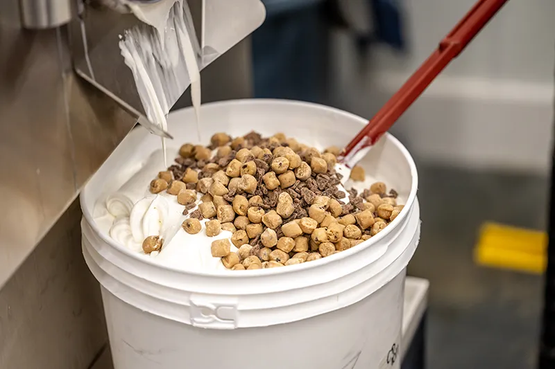 Mixing ice cream with cookie dough and chocolate chips in a large container for dessert preparation.